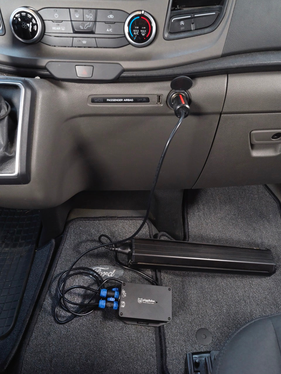 Piggibike liegt im Kfz Fußraum und ist an die 12V Buchse angeschlossen und lädt einen E-Bike Akku